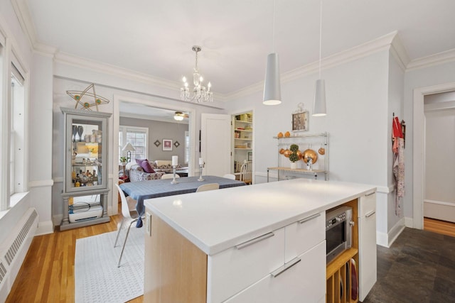 kitchen with radiator, decorative light fixtures, white cabinetry, wood-type flooring, and a center island