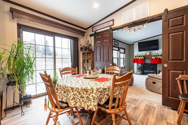 dining area with a barn door, lofted ceiling, ornamental molding, and light hardwood / wood-style flooring