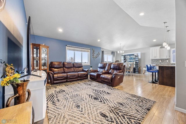 living room with light hardwood / wood-style floors, vaulted ceiling, and a notable chandelier