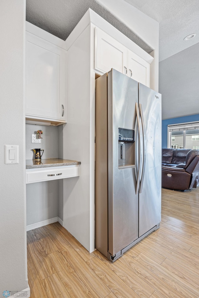 kitchen with white cabinets, stainless steel fridge, a textured ceiling, and light hardwood / wood-style floors