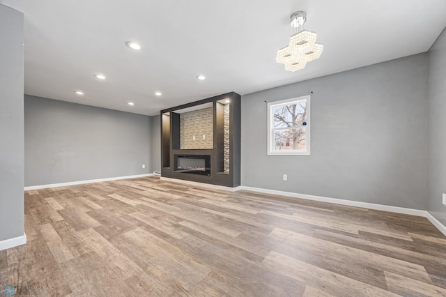 unfurnished living room with a large fireplace, light hardwood / wood-style floors, and an inviting chandelier