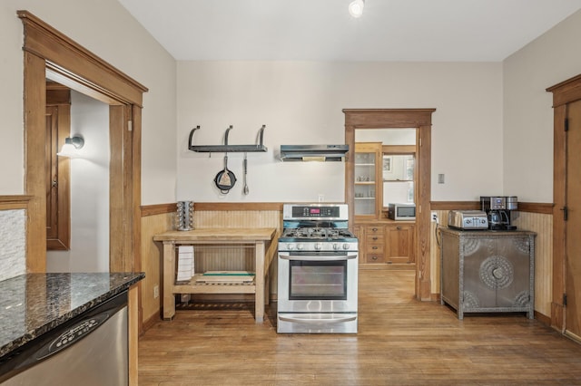 kitchen featuring extractor fan, wood walls, dark stone counters, stainless steel appliances, and light hardwood / wood-style floors