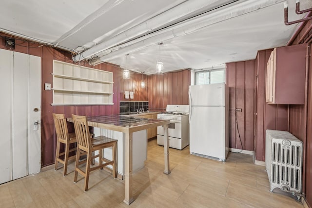 kitchen with white appliances, a breakfast bar area, radiator heating unit, tile countertops, and kitchen peninsula