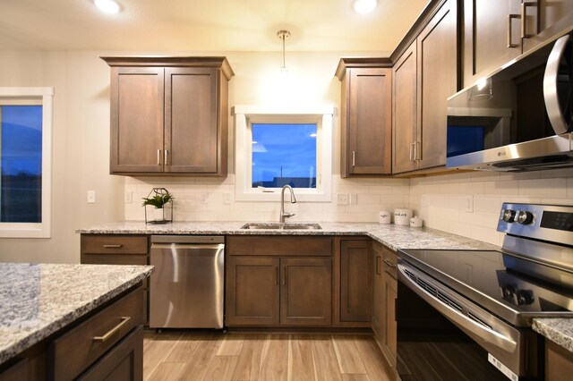 106 Fairway St, Zumbrota, MN 55992 - kitchen featuring appliances with stainless steel finishes, a sink, backsplash, light stone counters, and light wood-style floors