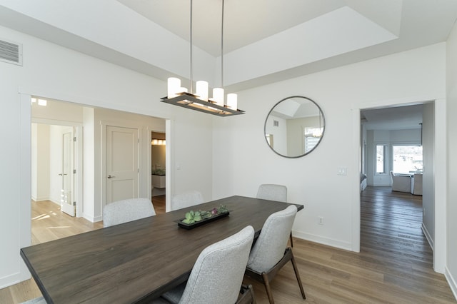 dining area featuring a chandelier, hardwood / wood-style flooring, and a raised ceiling