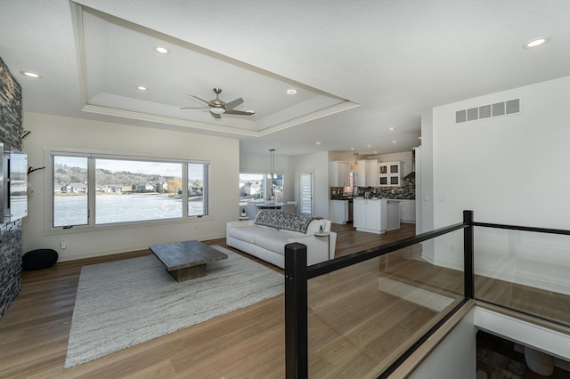 living room with wood-type flooring, a raised ceiling, ceiling fan, and crown molding