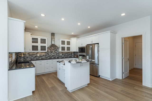 kitchen with white cabinetry, a center island, wall chimney exhaust hood, stainless steel appliances, and backsplash