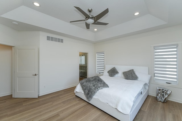 bedroom featuring ceiling fan, a raised ceiling, and light hardwood / wood-style flooring