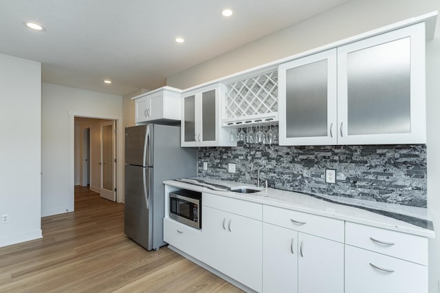 kitchen with light stone countertops, sink, stainless steel appliances, decorative backsplash, and white cabinets