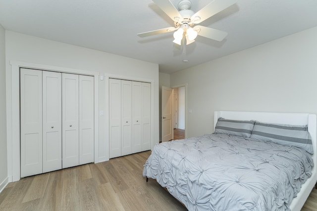 bedroom with light hardwood / wood-style floors, ceiling fan, and multiple closets