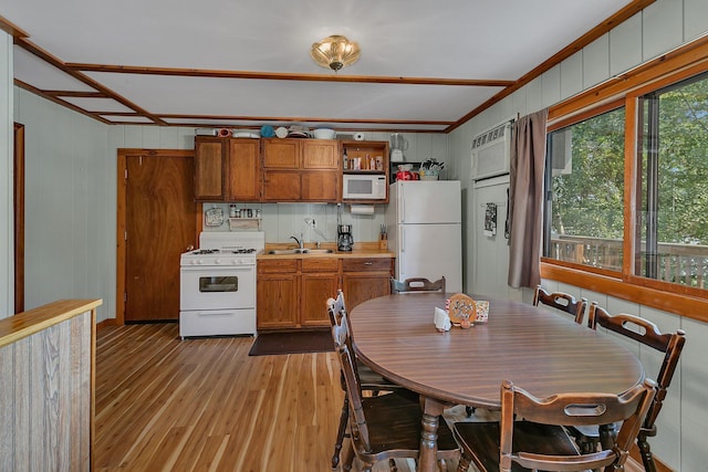 kitchen with light wood finished floors, light countertops, brown cabinets, white appliances, and a sink