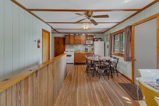 dining area with light wood-style flooring, wood walls, crown molding, and ceiling fan