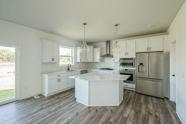 kitchen featuring white cabinetry, sink, wall chimney exhaust hood, stainless steel appliances, and decorative light fixtures