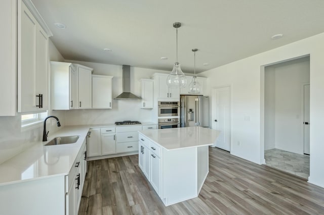 kitchen with wall chimney range hood, sink, appliances with stainless steel finishes, a kitchen island, and white cabinetry