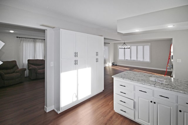 kitchen featuring light stone countertops, dark wood-type flooring, white cabinets, and hanging light fixtures