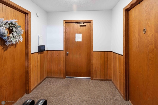 corridor with carpet flooring, a textured ceiling, and wood walls