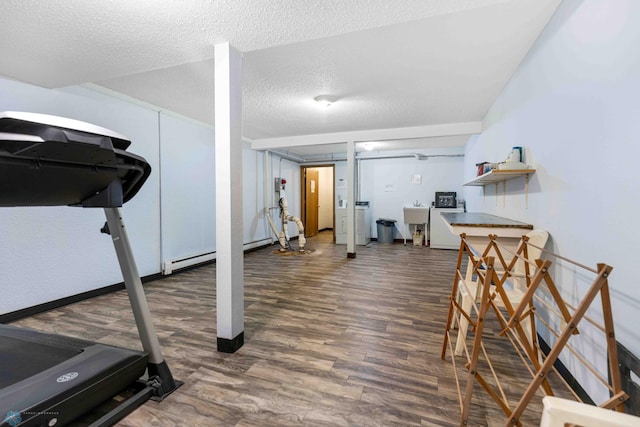 exercise room with sink, baseboard heating, a textured ceiling, dark hardwood / wood-style flooring, and washer / dryer