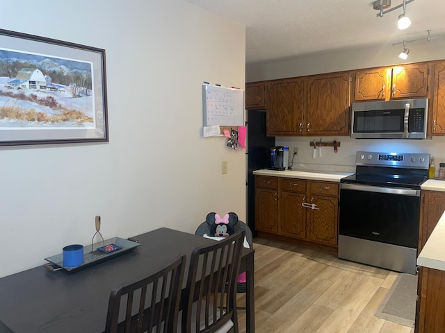 kitchen with appliances with stainless steel finishes, rail lighting, and light hardwood / wood-style flooring