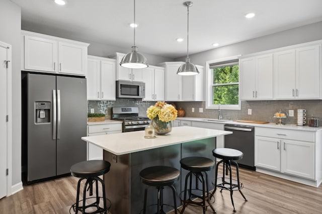 kitchen with stainless steel appliances, white cabinetry, hardwood / wood-style floors, and decorative light fixtures