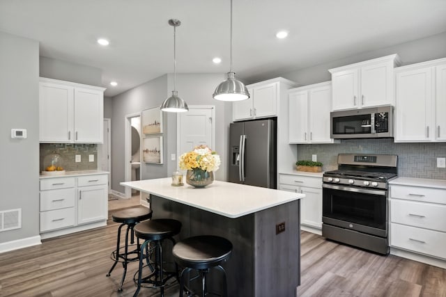 kitchen featuring stainless steel appliances, hanging light fixtures, white cabinets, and a kitchen bar