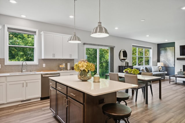 kitchen with pendant lighting, sink, white cabinetry, decorative backsplash, and stainless steel dishwasher