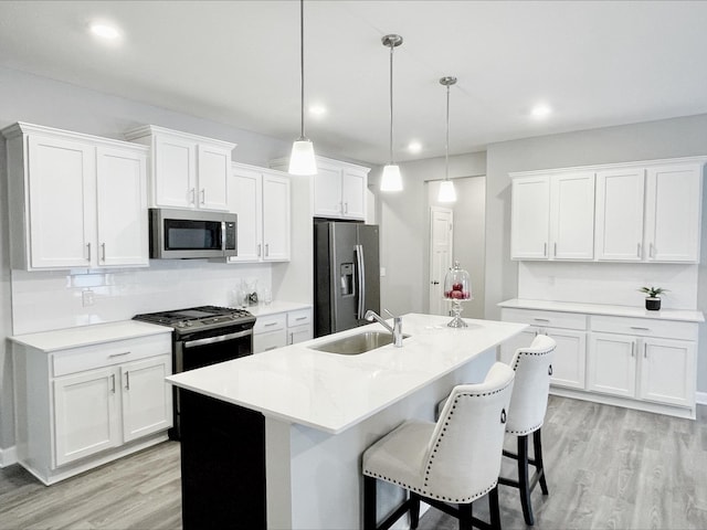 kitchen with pendant lighting, sink, light hardwood / wood-style flooring, appliances with stainless steel finishes, and white cabinetry