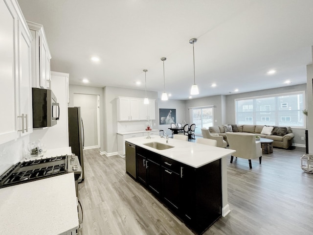 kitchen with a center island with sink, sink, appliances with stainless steel finishes, decorative light fixtures, and white cabinetry