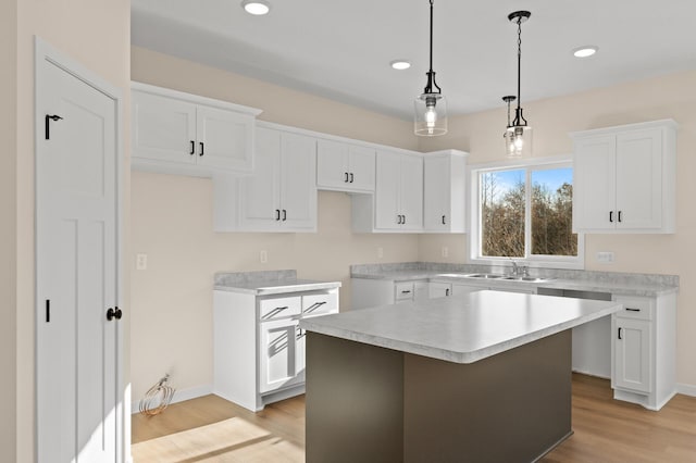 kitchen featuring sink, hanging light fixtures, a kitchen island, light hardwood / wood-style floors, and white cabinets