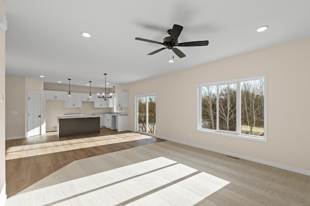 unfurnished living room featuring ceiling fan with notable chandelier and light hardwood / wood-style flooring