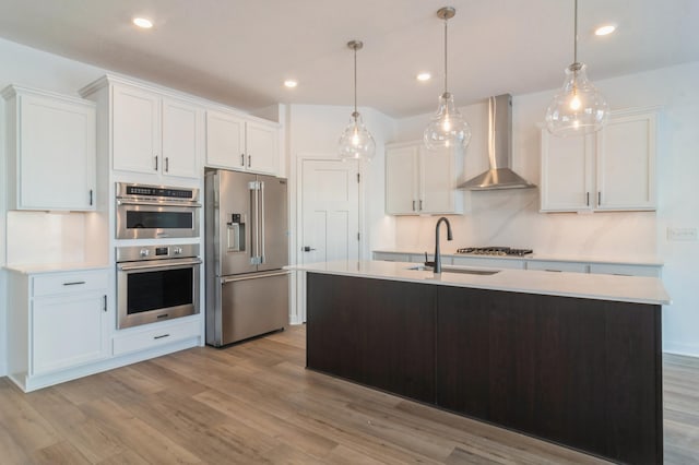 kitchen with appliances with stainless steel finishes, sink, wall chimney range hood, pendant lighting, and white cabinets