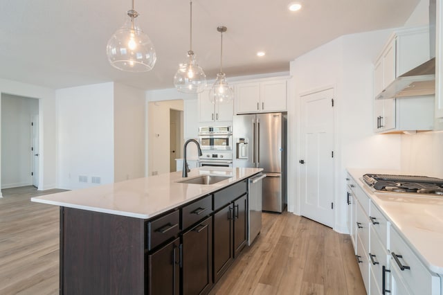 kitchen with a kitchen island with sink, wall chimney range hood, sink, white cabinetry, and stainless steel appliances