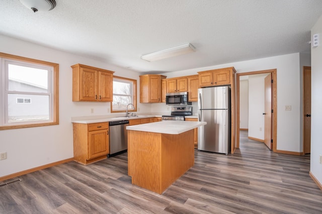 kitchen featuring appliances with stainless steel finishes, a textured ceiling, sink, a center island, and dark hardwood / wood-style floors