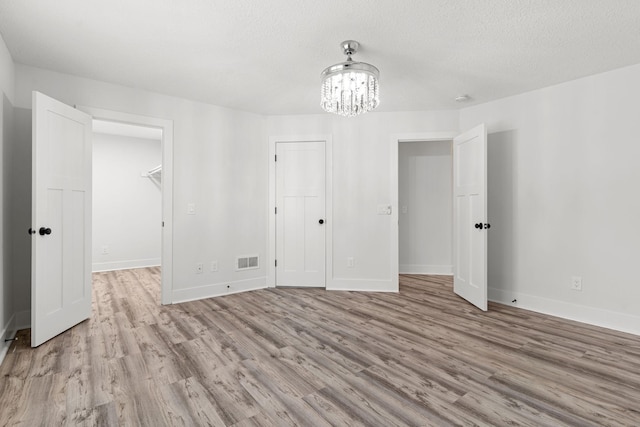 interior space with light wood-type flooring, a textured ceiling, and an inviting chandelier