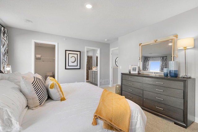 bedroom with a closet, light colored carpet, ensuite bath, and a spacious closet