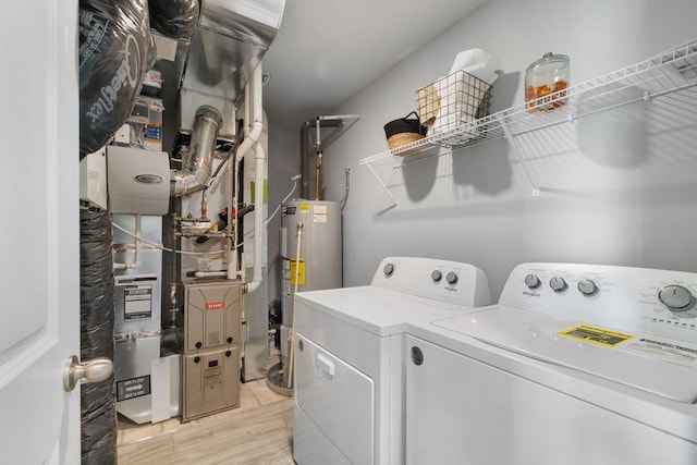 clothes washing area with light wood-type flooring, heating unit, washer and clothes dryer, and water heater