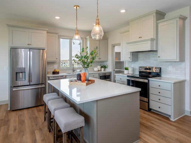 kitchen with sink, appliances with stainless steel finishes, pendant lighting, a kitchen island, and light wood-type flooring