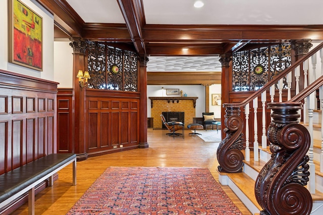 foyer featuring beam ceiling, a brick fireplace, decorative columns, light hardwood / wood-style floors, and ornamental molding