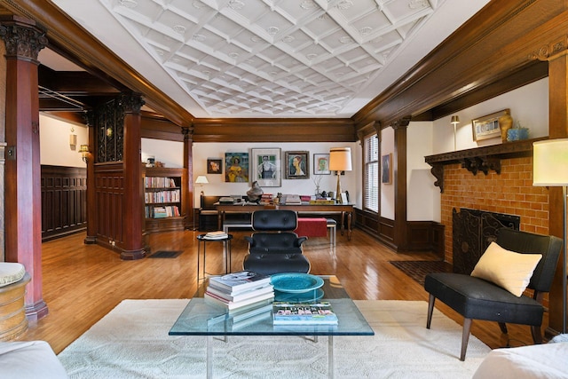 sitting room with hardwood / wood-style floors, a fireplace, ornate columns, and ornamental molding