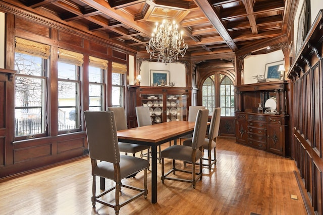 dining room with wood walls, a healthy amount of sunlight, light wood-type flooring, and coffered ceiling