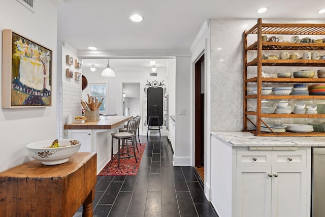 interior space with hanging light fixtures, ornamental molding, dark hardwood / wood-style flooring, white cabinetry, and a breakfast bar area