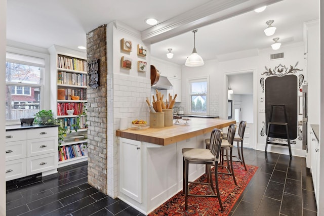 kitchen featuring a healthy amount of sunlight, butcher block counters, white cabinetry, and pendant lighting