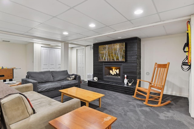 carpeted living room featuring a large fireplace and a drop ceiling