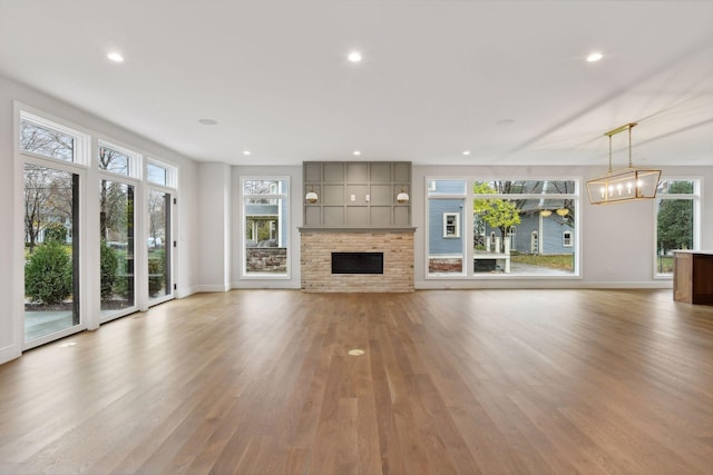 unfurnished living room featuring a fireplace, a chandelier, light hardwood / wood-style flooring, and a healthy amount of sunlight