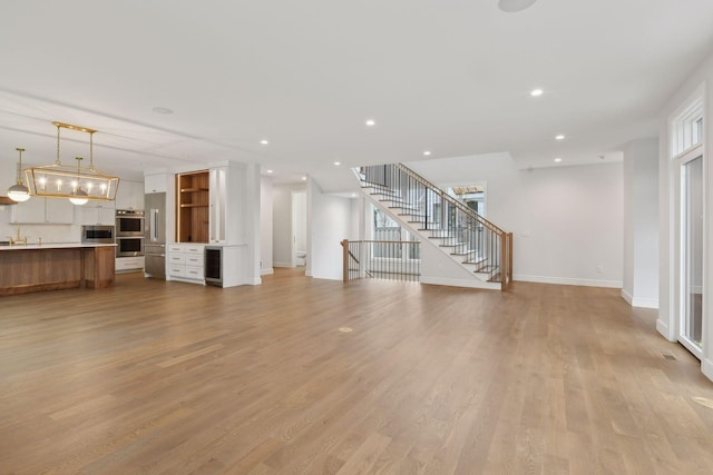 unfurnished living room featuring wine cooler and light hardwood / wood-style floors