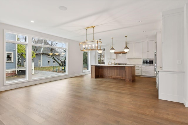 kitchen featuring hanging light fixtures, a center island with sink, white cabinets, dark hardwood / wood-style floors, and stainless steel microwave