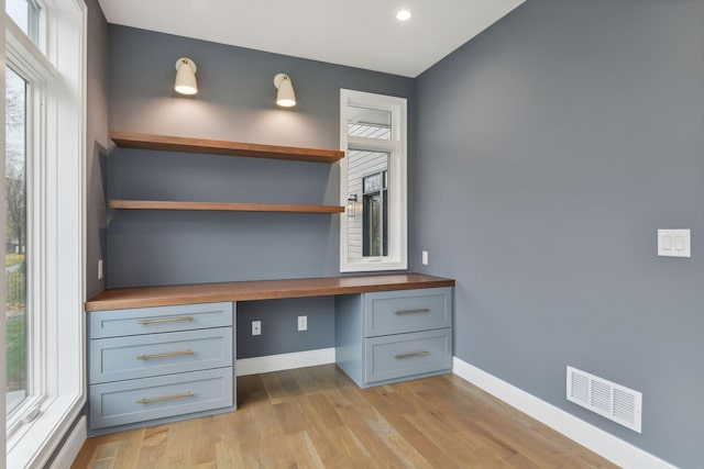 unfurnished office featuring built in desk, light hardwood / wood-style flooring, and a healthy amount of sunlight