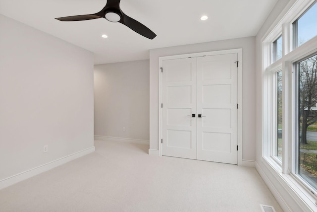 unfurnished bedroom featuring ceiling fan, a closet, light carpet, and multiple windows