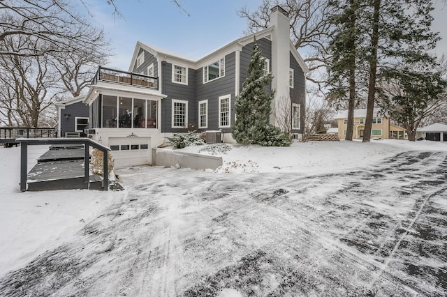 snow covered property with central air condition unit, a deck, a sunroom, a balcony, and a chimney