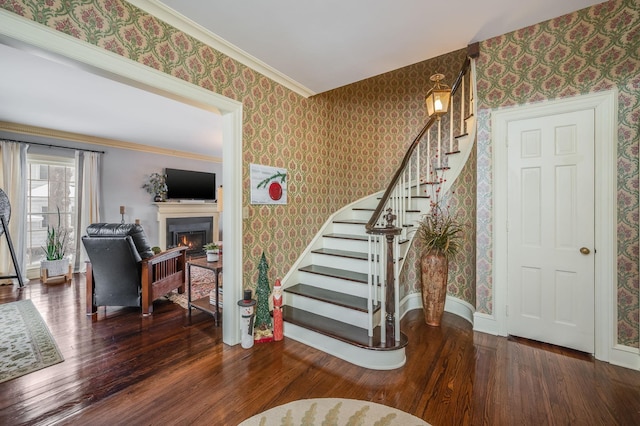 staircase with baseboards, a warm lit fireplace, wood finished floors, and wallpapered walls