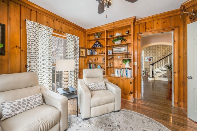 sitting room with stairway, wood walls, built in features, wood finished floors, and a ceiling fan